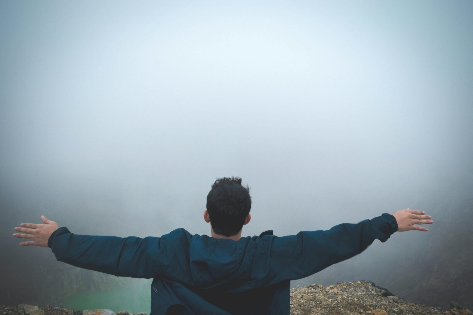 A man stands on a foggy cliff with arms outstretched, embracing freedom and nature.