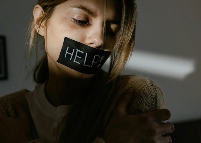 Distressed and traumatized woman with 'HELP' on mouth in moody lighting, symbolizing silence, sadness, and pressure.